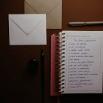 Overhead view of a to-do list notebook with New Year's resolutions, pens, and envelopes on a desk.