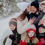 A joyful family enjoying a snowy day in a forest, wrapped in warm clothing.